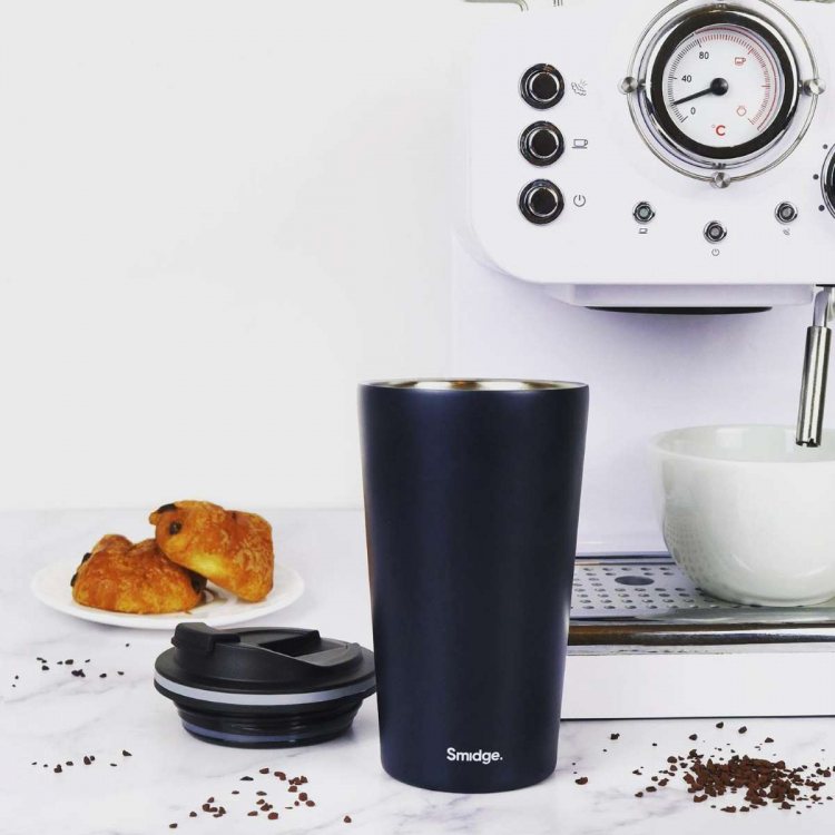 Photo showing the black Smidge Reusable Travel Cup on a white marble surface, with a coffee machine 