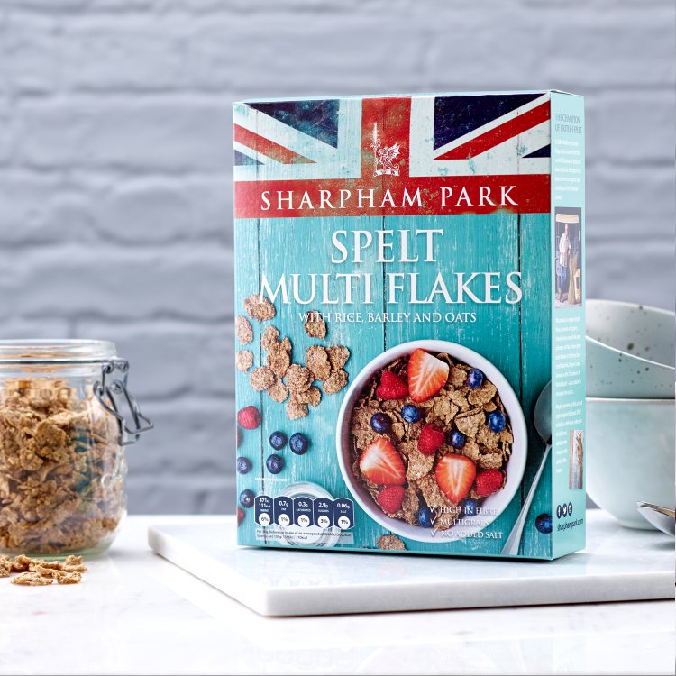 Photo showing the Sharpham Park Spelt Multi Flakes cereals in a box on a white surface with a glass